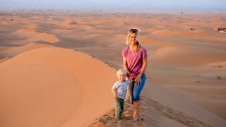 Reisejournalistin Astrid Därr steht mit ihrem Sohn auf einen Düne, im Hintergrund sieht man die Sahara-Wüste.  In SWR1 Leute verrät sie, warum Reisen für die Entwicklung von Kindern wichtig sind, gibt Reisetipps für Vanlife und Nahziele und wie die Reisetrends 2024 aussehen.