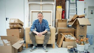 Der Maler Norbert Bisky sitzt auf einem Sofa in seinem Atelier. Norbert Bisky ist einer der wichtigsten zeitgenössischen deutschen Künstler, seine Werke sind in den bedeutendsten Museen der Welt zu sehen etwa dem MOMA in New York. Er verbindet Gemälde- und Bühnenkunst.