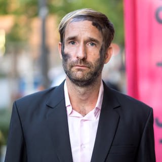 Philipp Ruch, Begründer des Zentrums für Politische Schönheit, steht vor Beginn einer Veranstaltung des Kunstfestes 2019 zum Umgang mit der Holocaust-Erinnerung vor einem Banner.