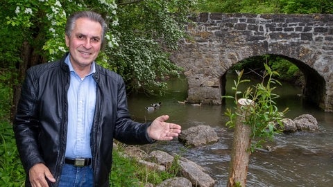 Naturschützer Claus-Peter Hutter zeigt mit der Hand auf einem Bach mit einer Steinbrücke.