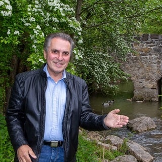 Naturschützer Claus-Peter Hutter zeigt mit der Hand auf einem Bach mit einer Steinbrücke.