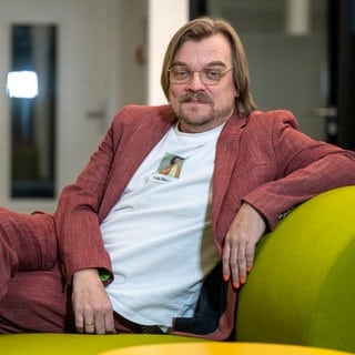 Nilz Bokelberg sitzt auf einem Sofa bei einer Talkrunde.