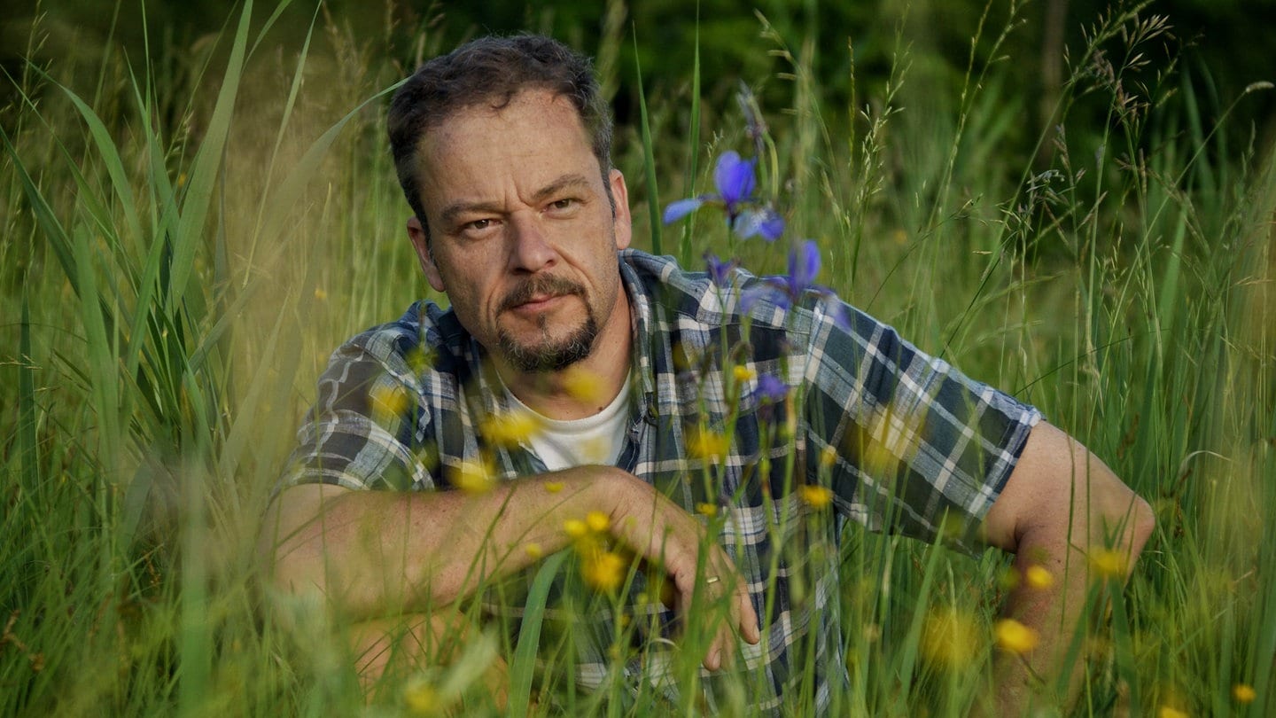 Naturfilmer und -schützer Jan Haft sitzt in der Hocke in einer blühenden Wiese.