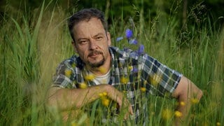 Naturfilmer und -schützer Jan Haft sitzt in der Hocke in einer blühenden Wiese.