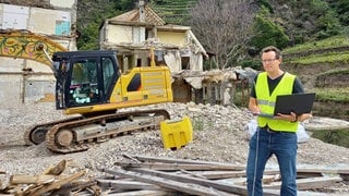 Prof. Jörn Birkmann steht im Ahrtal vor einem Schutthaufen. Im Hintergrund ein Bagger und ein von der Flut zerstörtes Haus.  In SWR1 Leute sprechen wir mit ihm über Extremwetter und Naturkatastrophen: Prof. Birkmann von der Uni Stuttgart sucht nach Strategien, wie wir uns in Zeiten des Klimawandels besser schützen und vorbereiten können.