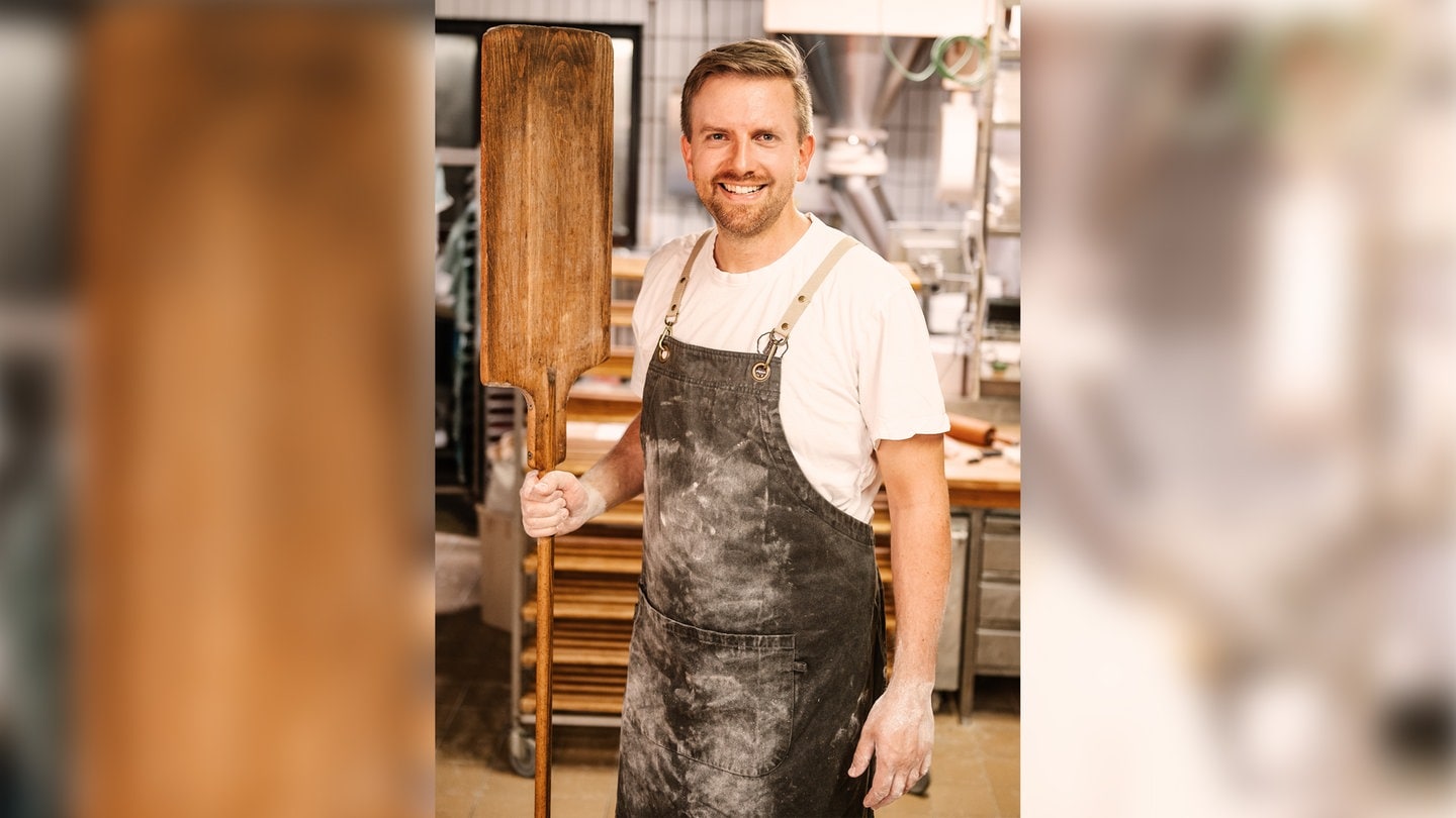 Ingmar Krimmer, Bäcker des Jahres 2024, steht mit bemehlten Händen und Schürze in der Backstube und hält einen Brotschieber in der rechten Hand.