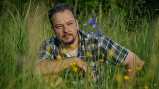 Naturfilmer und -schützer Jan Haft sitzt in der Hocke in einer blühenden Wiese.