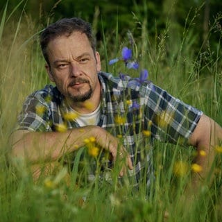 Naturfilmer und -schützer Jan Haft sitzt in der Hocke in einer blühenden Wiese.