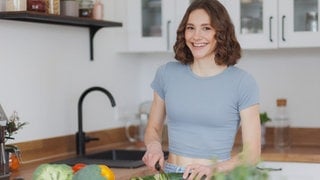 Foodbloggerin Maya Leinenbach schneidet eine Gurke und lächelt in die Kamera.