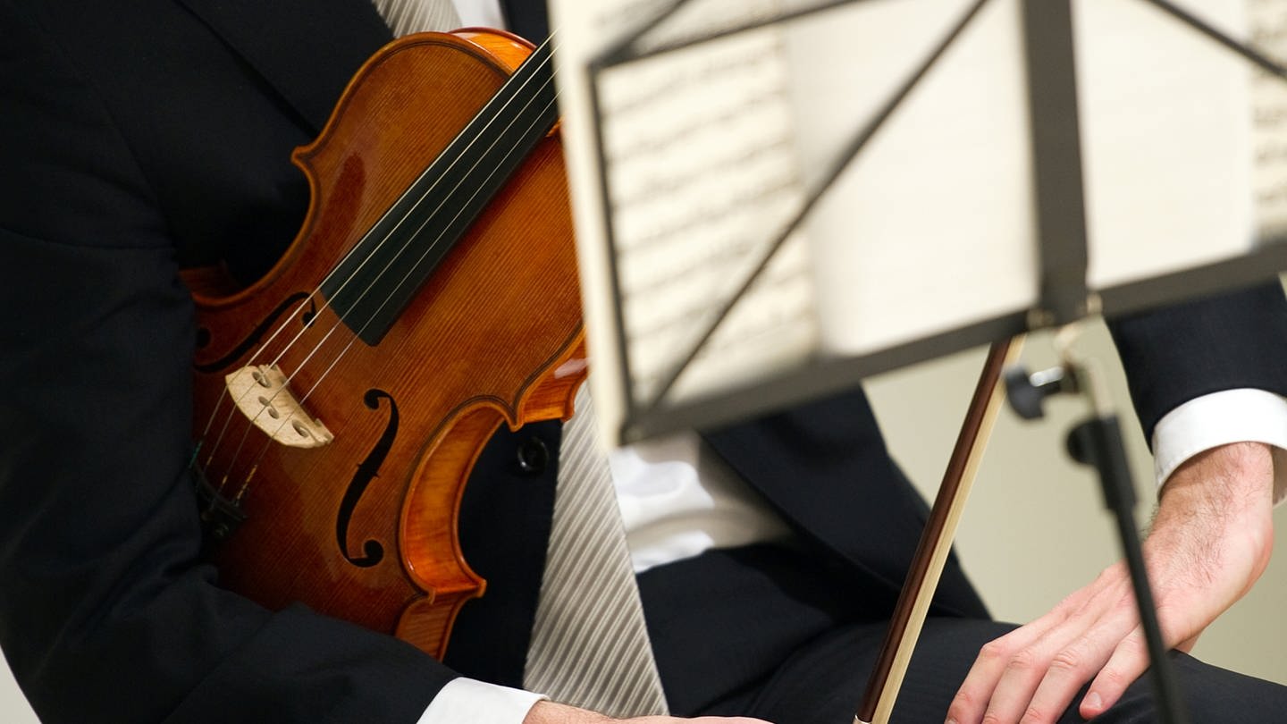 Ein Geiger sitzt mit seiner Violine hinter einem Notenständer.