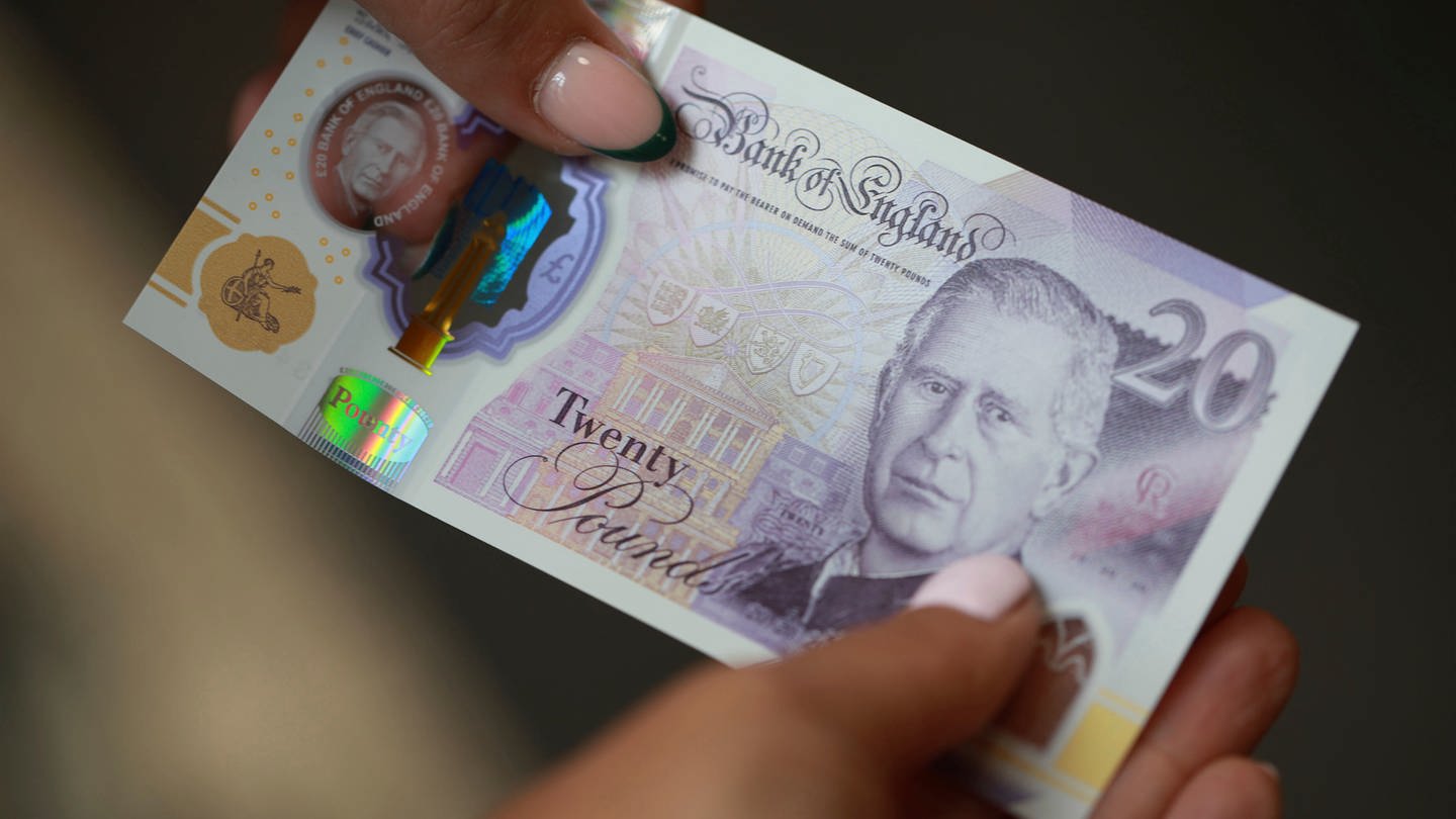Ein Mensch mit rosa Nagellack hält eine 20-er Banknote in den Händen. Darauf ist König Charles abgebildet.
