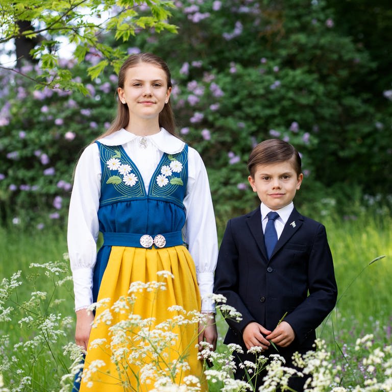 Prinzessin Estelle und Prinz Oscar posieren in traditioneller Tracht und Anzug auf einer grünen Wiese für den schwedischen Nationalfeiertag.