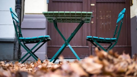 Stühle und Tisch im Herbstlaub: Als Eselsbrücke helfen bei der Zeitumstellung die Gartenstühle. Bei der Umstellung auf die Winterzeit müssen sie zurück ins Haus, also stellen wir auch die Uhr zurück.