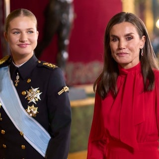 Königin Letizia von Spanien trägt ihr dunkles Haar offen und ein schickes rotes Kleid. Neben ihr läuft ihre Tochter in Militäruniform und streng zurückgebundenem Zopf, denn die Thronfolgerin Leonor von Spanien macht derzeit eine Ausbildung beim Spanischen Militär.