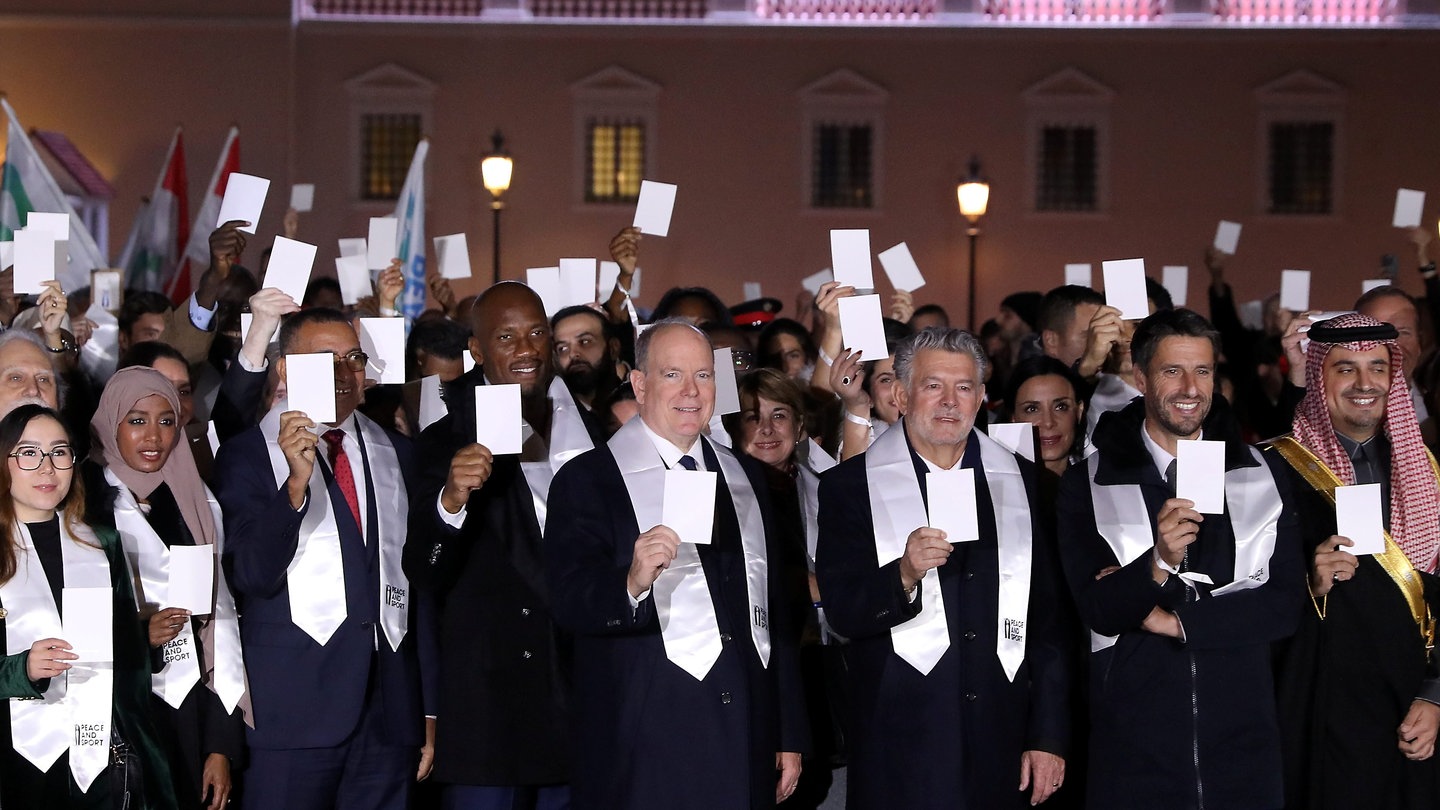 Ein Gruppenbild mit Albert, dem Fürsten von Monaco, der im schwarzen Anzug in der Mitte steht, alle Leute auf dem Bild halten einen weißen Zettel hoch und tragen eine weiße Stola um den Hals