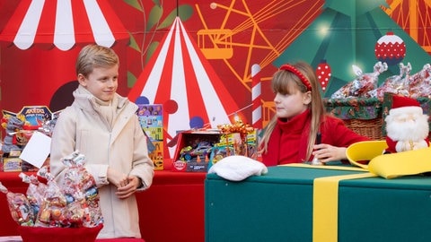 Prinzessin Gabriella und Prinz Jacques von Monaco verteilen im Hof des Fürstenpalastes traditionelle Weihnachtsgeschenke an monegassische Kinder und stehen in weihnachtlicher Kulisse. Gabriella hält ein Glöckchen.