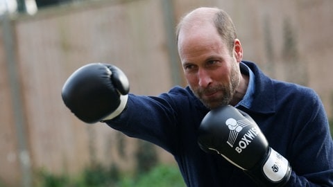 Prinz William trägt Boxhandschuhe und boxt damit konzentriert in die Luft. Er trägt eine dunkelblaue Jacke dazu.