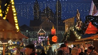 Besucher laufen vor der Kulisse des Kaiserdoms über den Weihnachtsmarkt in Speyer