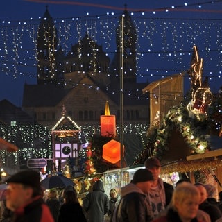 Besucher laufen vor der Kulisse des Kaiserdoms über den Weihnachtsmarkt in Speyer