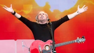 Barry Gibb von den Bee Gees tritt mit Gitarre und erhobenen Armen auf der Bühne auf