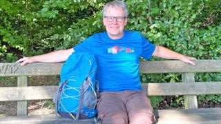SWR4 Moderator Holger Bentzien sitzt bei einer Rast auf Wanderung, den Rucksack neben sich