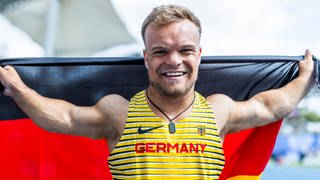 Kugekstoßer und Olympiasportler Niko Kappel im Deutschlandtrikot. Er hält eine Deutschlandfahne hoch.