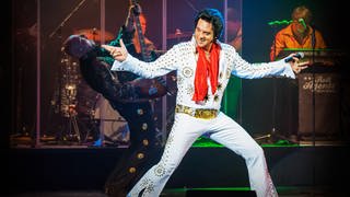 Der Darsteller des Musicals in einem weißen Elvis Kostüm singend auf der Bühne