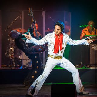 Der Darsteller des Musicals in einem weißen Elvis Kostüm singend auf der Bühne