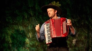 Musiker und Kabarettist Martin Wangler steht als Fidelius Waldvogel auf der Bühne – mit Akkordeon und einem Hut im Schwarzwald-Stil.