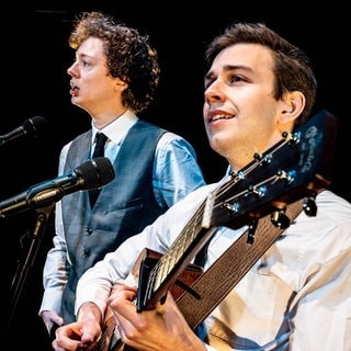 Die Sänger und Musiker der Simon and Garfunkel Story singen am Mikrofon und einer spielt Gitarre