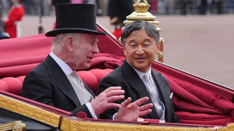 König Charles und Kaiser Naruhito sitzen in einer Kutsche und unterhalten sich gut gelaunt.