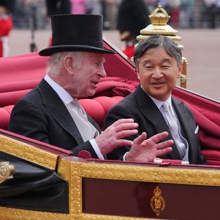 König Charles und Kaiser Naruhito sitzen in einer Kutsche und unterhalten sich gut gelaunt.