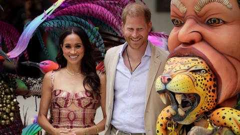 Prinz Harry und Herzogin Meghan zu Besuch in Kolumbien. Neben ihnen sind zwei Masken des Kunstzentrums "Zapata".