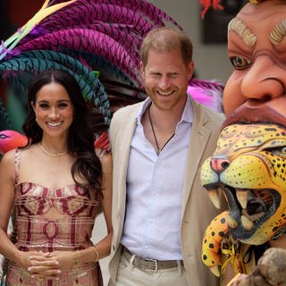 Prinz Harry und Herzogin Meghan zu Besuch in Kolumbien. Neben ihnen sind zwei Masken des Kunstzentrums "Zapata".