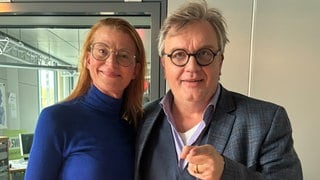 Annelies Royale Welt: Die Moderatorin spricht im SWR4 Studio mit Hape Kerkeling über seine verwandtschaftliche Beziehung zu König Charles. Beide schauen freundlich in die Kamera.