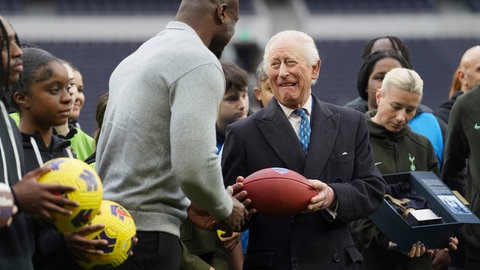 König Charles witzelt mit dem Football-Star Efe Obada rum und hält einen Football in der Hand.