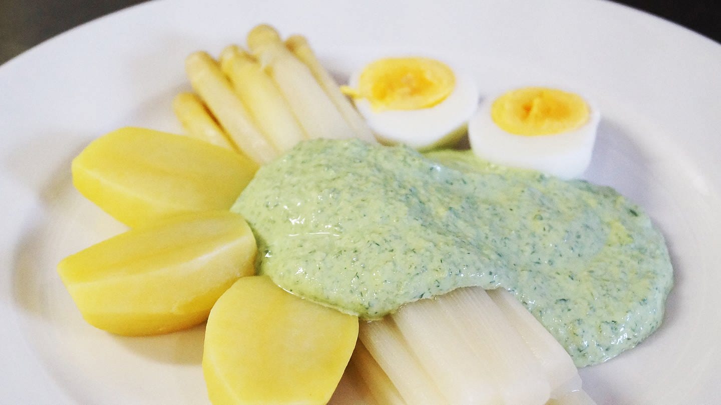 weißer Teller mit Stangenspargel mit grüner Soße, dazu Kartoffeln und zwei hartgekochte Eier