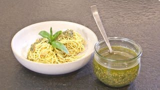 Teller Pasta mit Pesto, daneben Glas Pesto mit Löffel darin