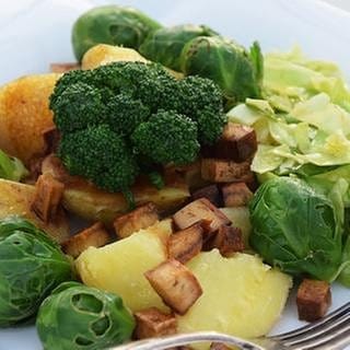 weißer, eckiger teller mit salat aus Kartoffeln, rosenkohl, broccoli und tofu mit einer gabel