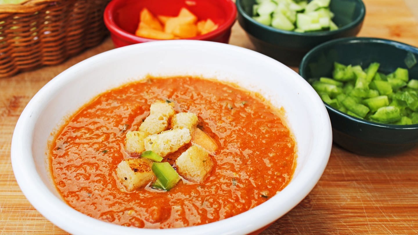 Schale mit kalter, roter Suppe mit Croutons als Einlage. Dahinter Schalen mit verschiedenem Gemüse