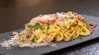 Rezept: Original Spaghetti alla Carbonara angerichtet mit Parmesan auf einer Schieferplatte.