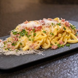 Rezept: Original Spaghetti alla Carbonara angerichtet mit Parmesan auf einer Schieferplatte.
