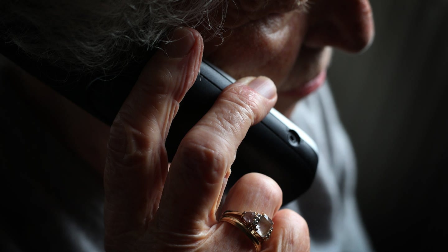 Eine ältere Frau hält vor dunklem Hintergrund den Telefonhörer ans Ohr