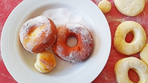 Krapfen mit Zucker auf einem weißen Teller, drumherum Hefeteilchen und Kringel ohne Zucker