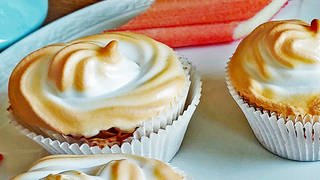 Rhabarber-Muffins mit Baiserhaube auf weißem Teller. Drumherum Stücke von Rhabarber.