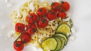 Bandnudeln mit Feta und gegrillten Tomaten und Zucchini auf einem eckigen, weißen Teller