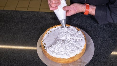 Mit einer Sterntülle wird der Eischnee so auf den Rhabarberkuchen gespritzt, dass einzelnen Stücke aus Baiser entstehen.