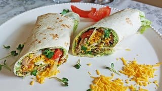 ein Wrap, aufgeschnitten, mit Huhn, Guacamole und Salat und geriebenem Käse auf einem weißen Teller