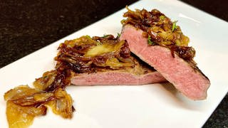 Zwiebelrostbraten schön saftig und zart aus Rind mit einem rosa Kern. Angerichtet auf einem Teller.