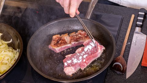 Ein weiterer Schritt im Rezept: Die Scheiben vom Rind für den Zwiebelrostbraten werden in einer Pfanne mit Butterschmalz angebraten. So wird das Fleisch saftig und zart.